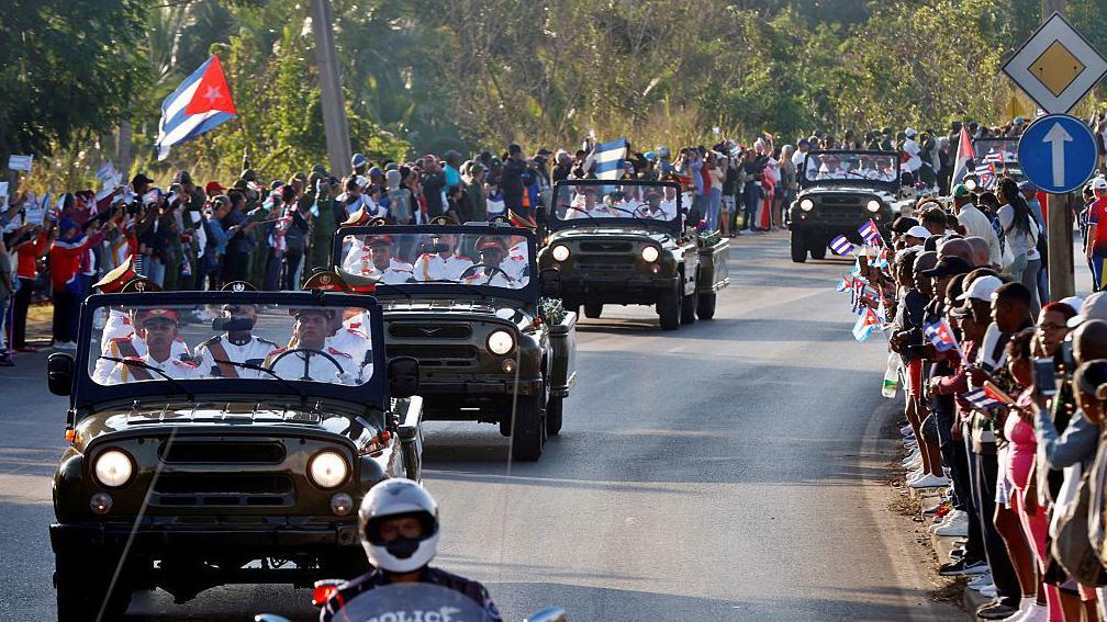 Una multitud alineada a lo largo de una avenida ondea banderas cubanas mientras una caravana militar pasa con los restos de los soldados muertos en Venezuela