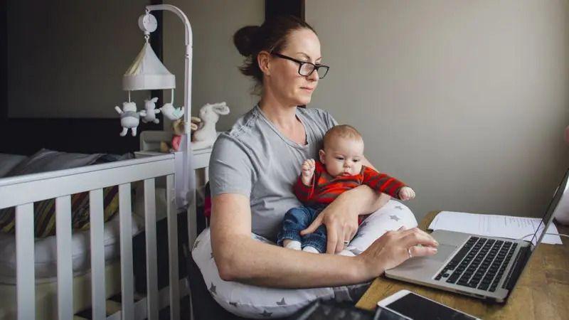 Žena jednom rukom drži bebu, drugom radi na laptopu