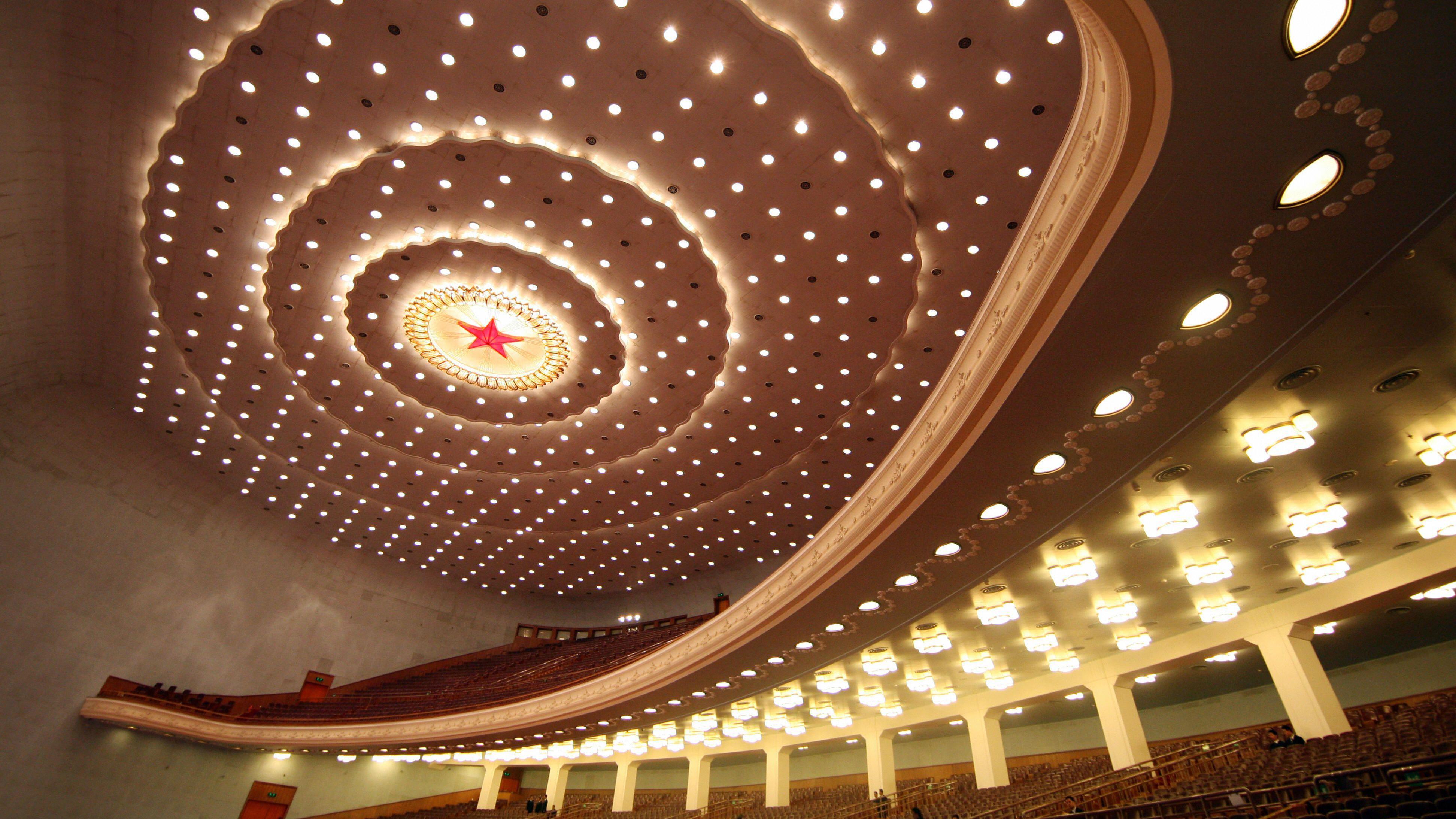 Una fotografía tomada al interior de un auditorio, mirando hacia un techo repleto de luces circulares blancas y una estrella roja con un círculo iluminado en el centro; se aprecian filas de asientos dispuestas en varios niveles.