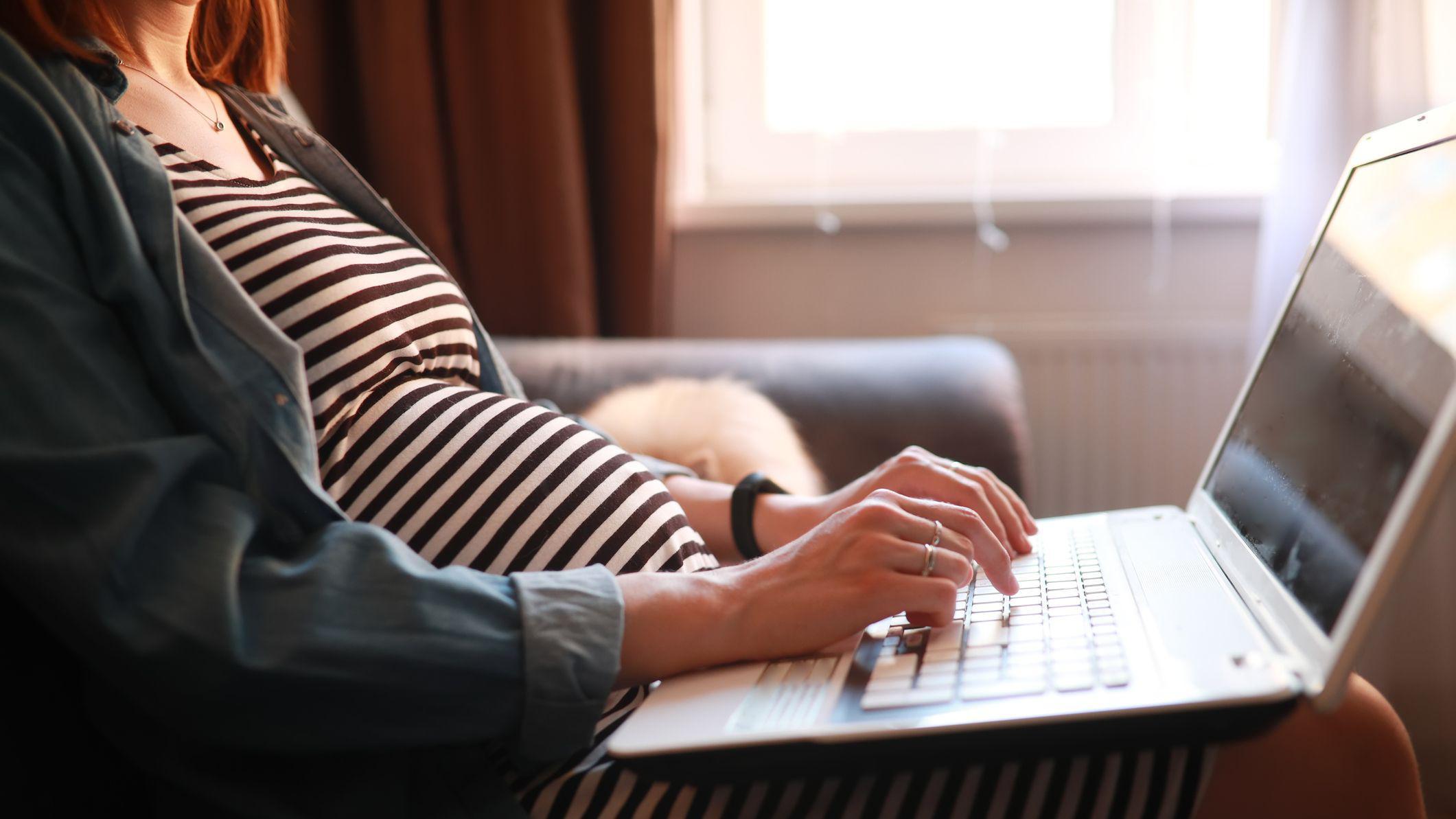 Jovem grávida usando um laptop apoiado no colo