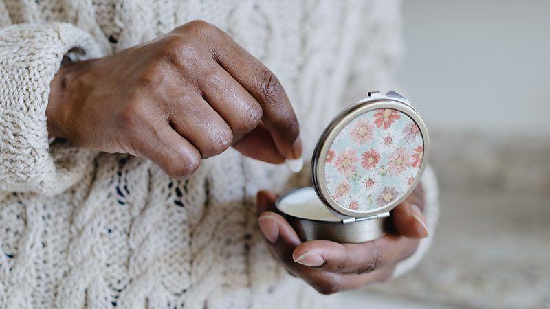 Pessoa com casaco branco retira um comprimido de um recipiente