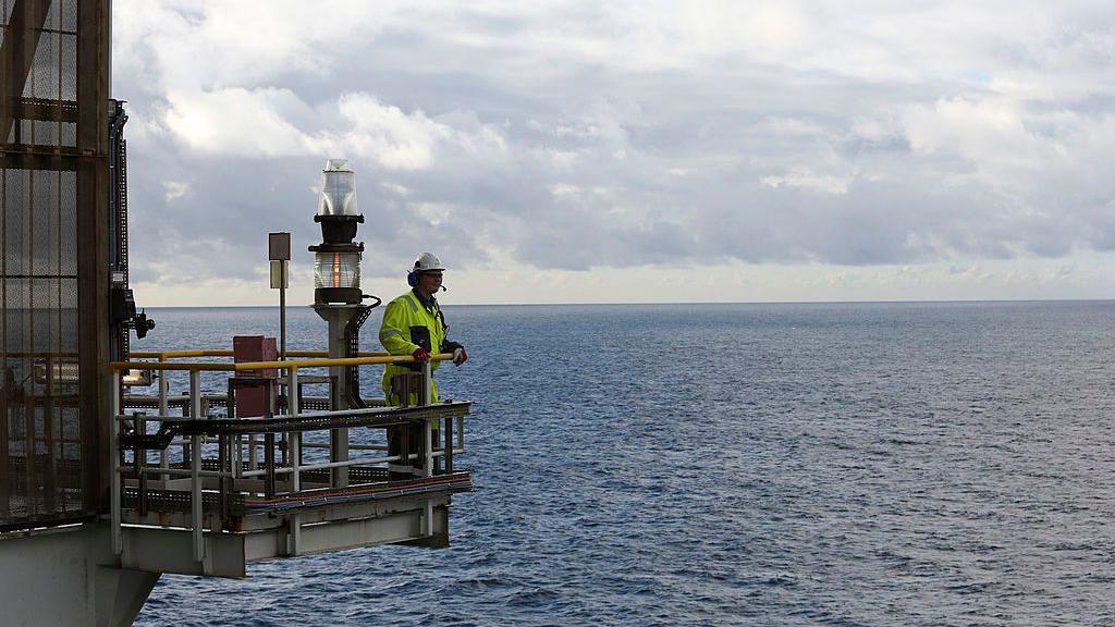 Un hombre observa la lejanía en un saliente de una plataforma en el mar. 