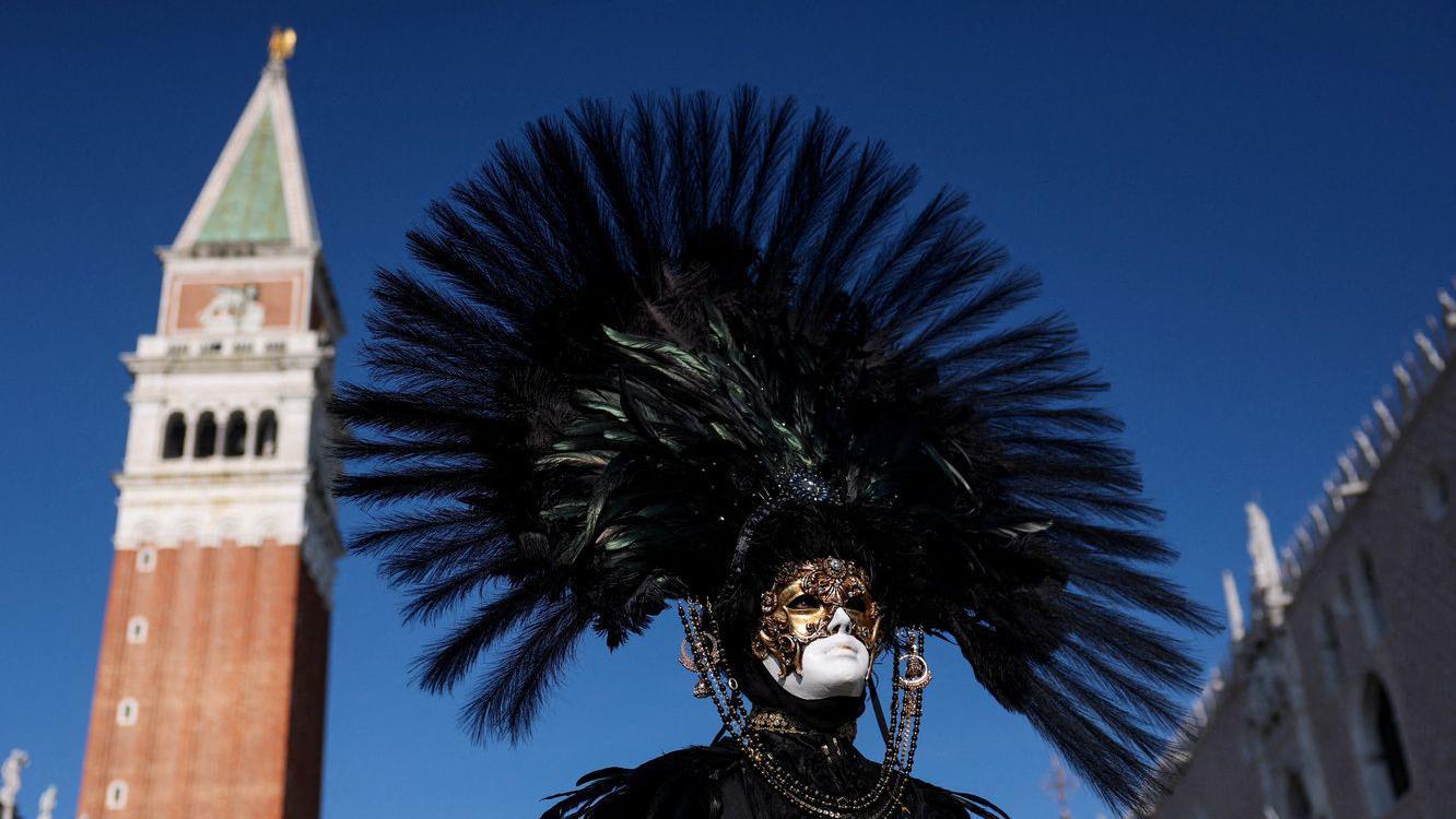 Čovek na licu ima paunovo perje iza se vidi toranj crkve Svetog Marka u Italiji