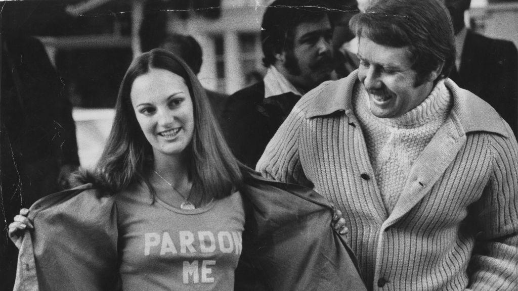 Patty Hearst junto a su esposo, se abre su chaqueta para revelar una camiseta que dice "Perdónenme"