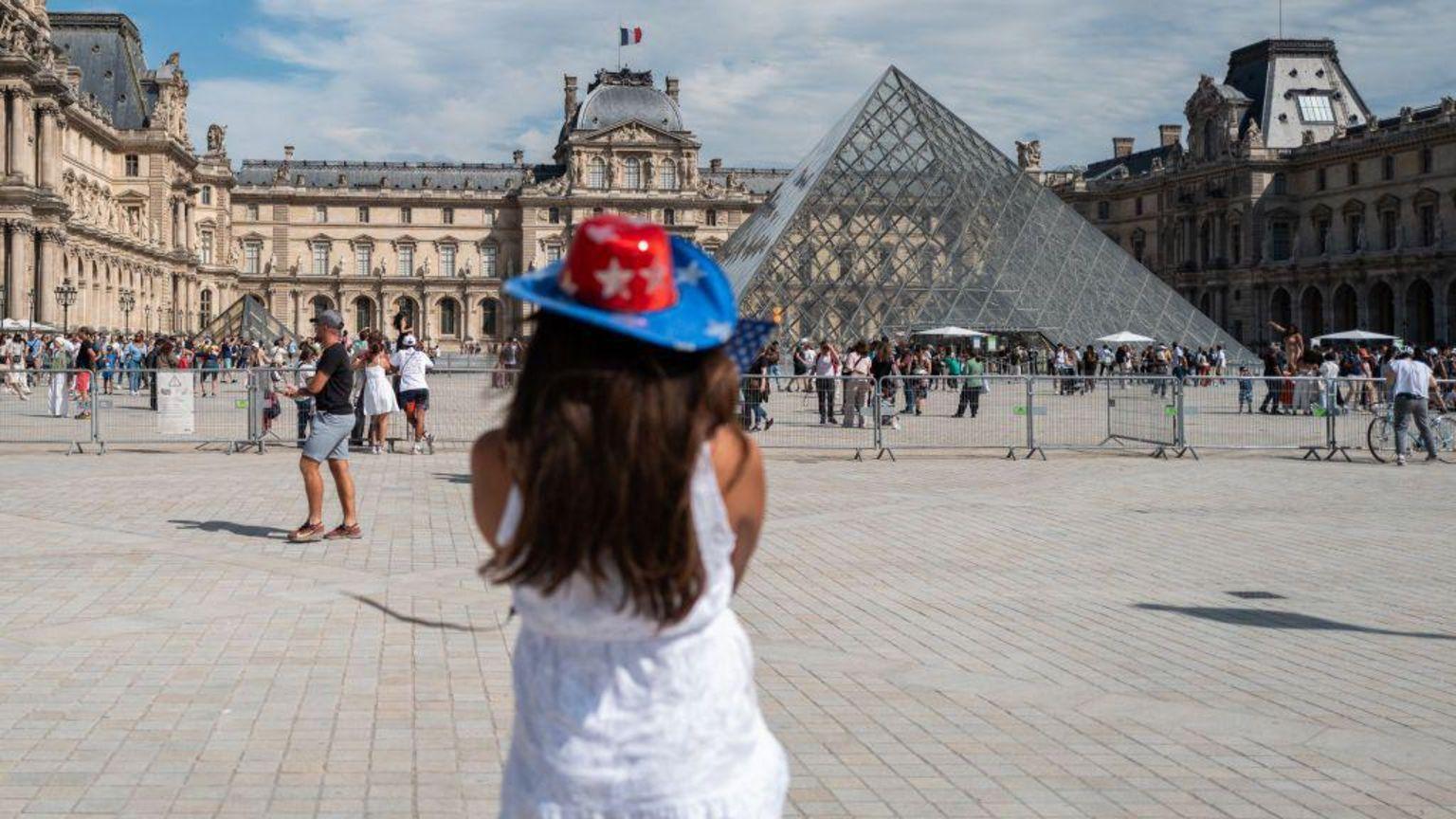 Una mujer, frente al Museo del Louvre, con otros turistas alrededor. 