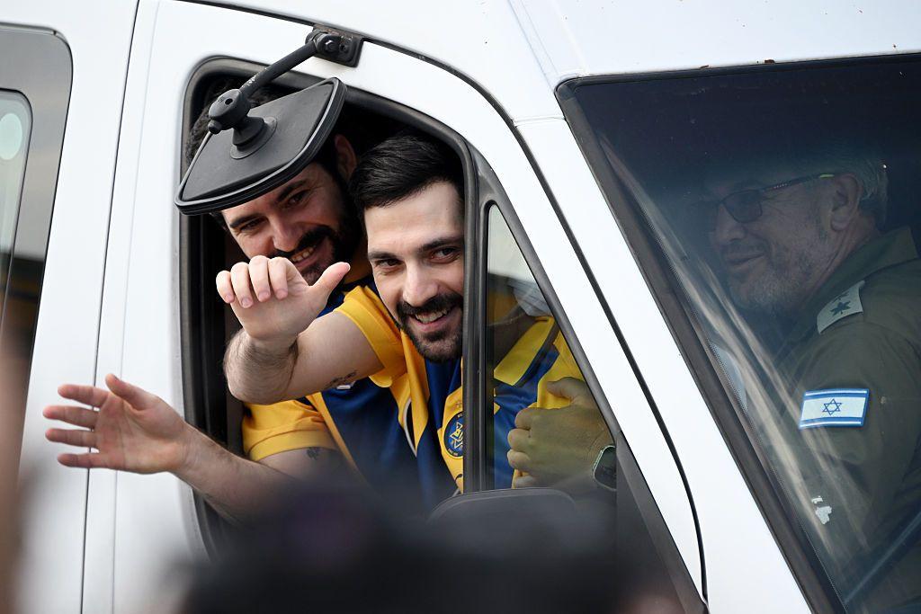Los rehenes israelíes Ziv y Gali Berman, saludan a sus seguidores dentro de un auto. Apenas se les ve la cara y los brazos saludando. Ambos van con una camiseta deportiva de color amarillo y azul oscuro. A su lado, dentro del vehículo, se ve a alguien que pareciera ser de las fuerzas armadas de Israel, pues va de uniforme verde olivo.