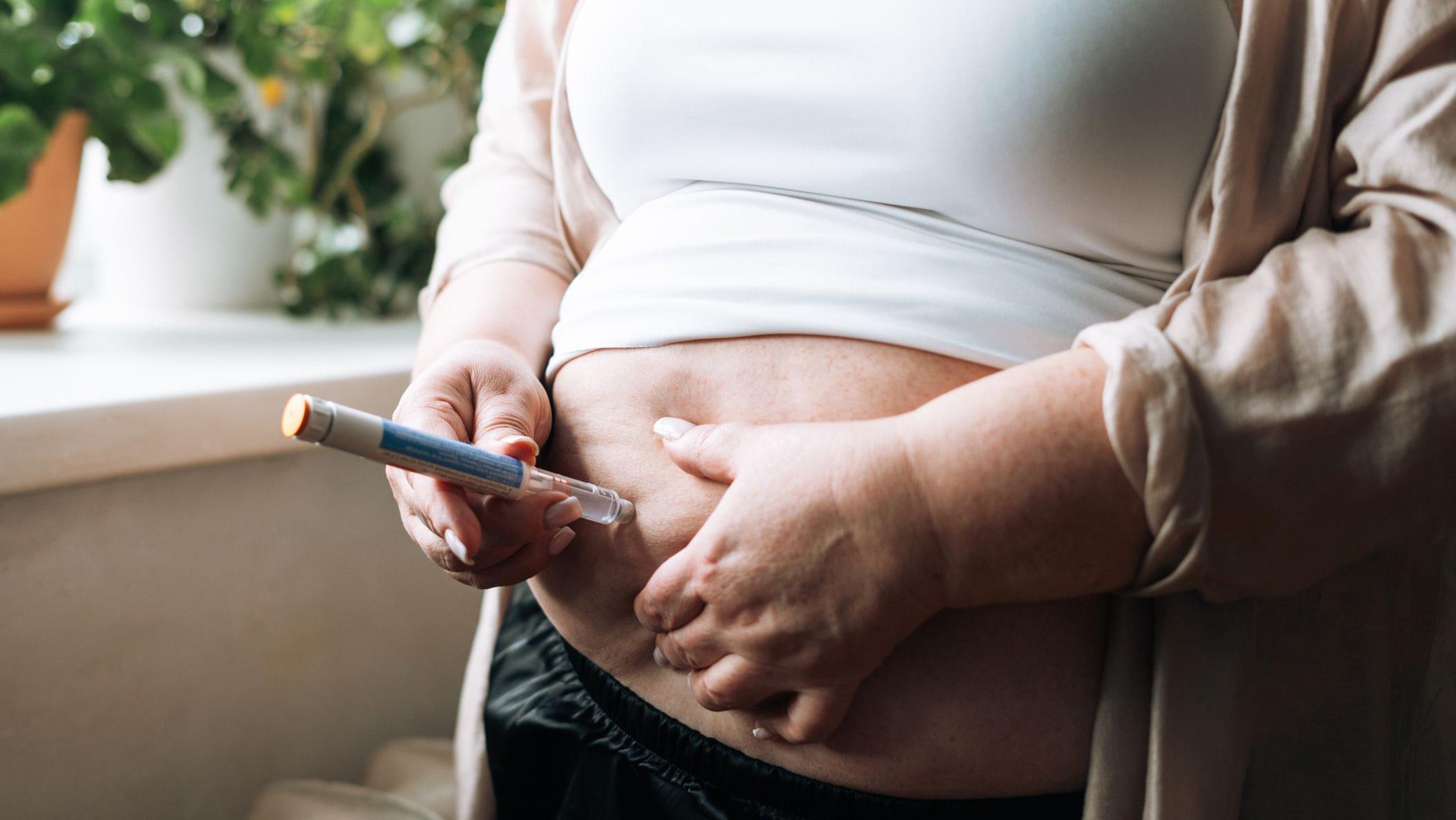 Una mujer con sobrepeso cuyo rostro no vemos se inyecta una pluma de Ozempic en el abdomen.