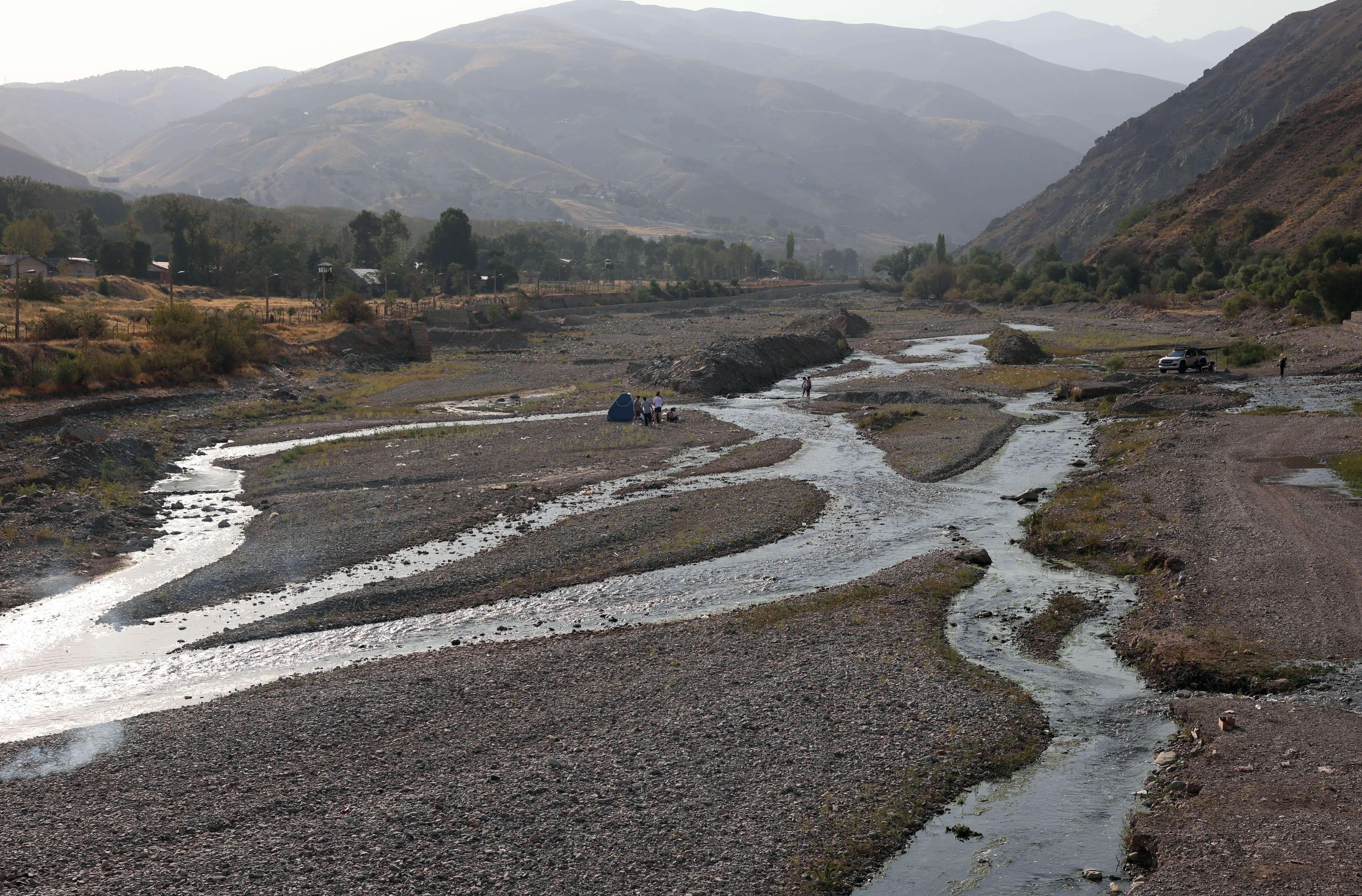 Iraníes hacen un picnic en un río casi seco, que alguna vez estuvo lleno, en el área de Fasham, al norte de Teherán, el 25 de agosto de 2025 - varias corrientes de agua corren por el lecho seco del río.