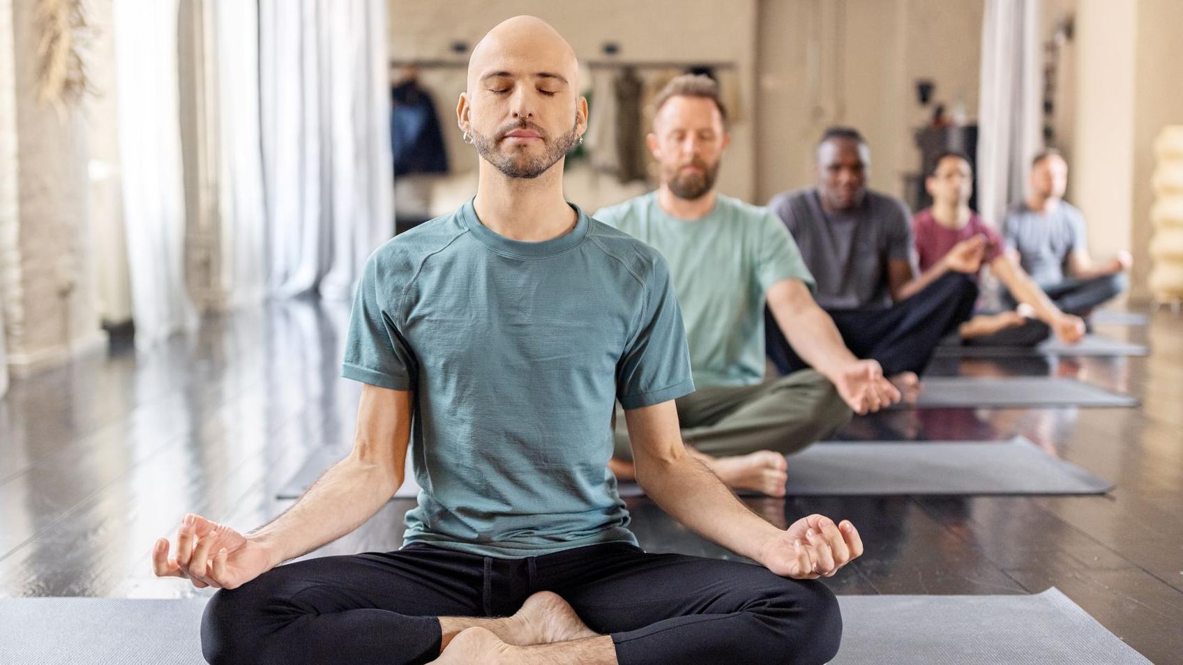 Grupo de personas meditando en la postura del loto padmasana en una clase de yoga.