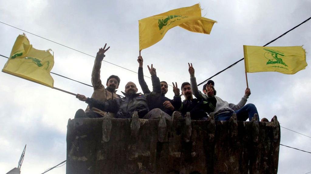 Para pria mengibarkan bendera Hezbollah ketika mereka tiba di kota Nabatieh, Lebanon selatan, pada 2024