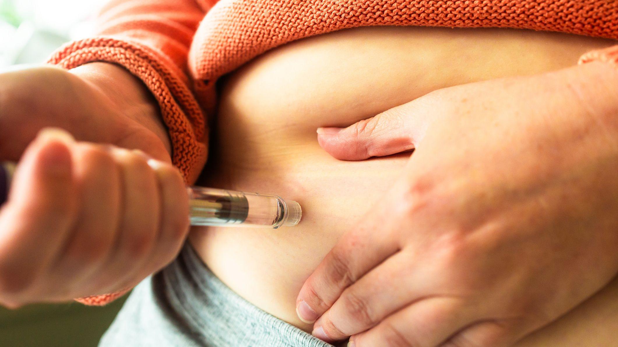 特寫鏡頭拍攝一名女士的手，她正拿著一支減肥注射筆，準備將藥物注射到腹部。