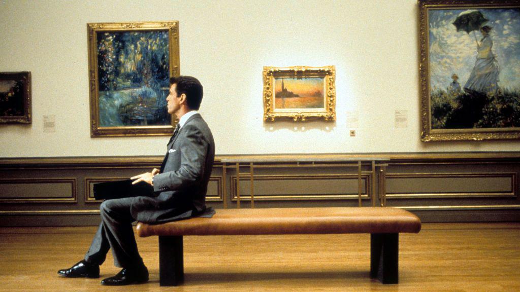 Cena do filme 'Thomas Crown: A Arte do Crime', com Pierce Brosnan sentado em uma galeria de arte