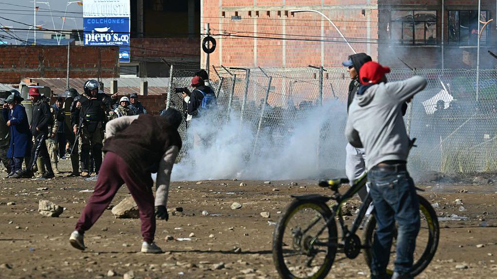La policía se enfrenta a varias personas que recogen piedras del suelo. 