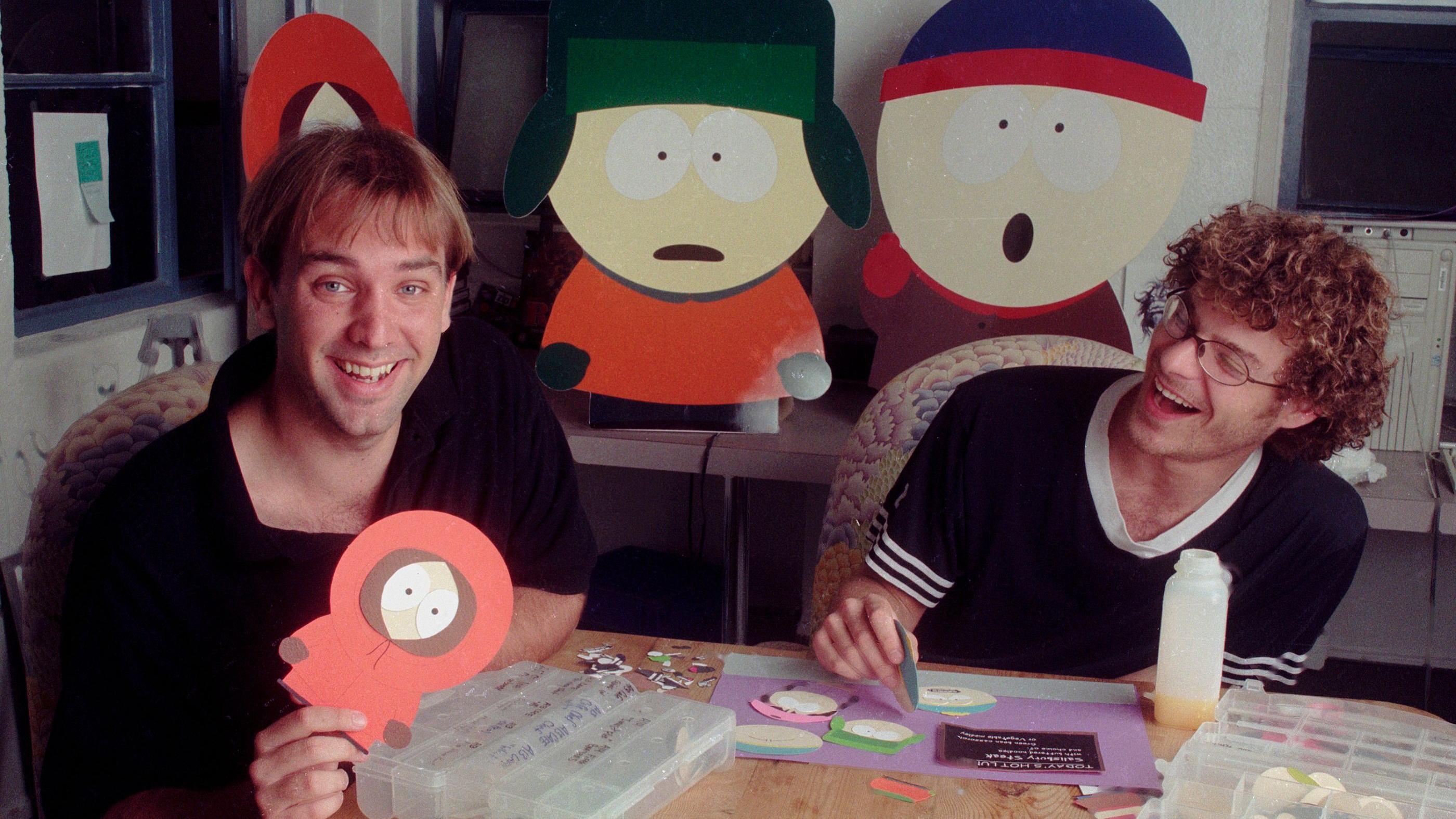 Trey Parker y Matt Stone fotografiados con sus personajes hechos de cartón en 1997, donde ambos aparecen sonriendo