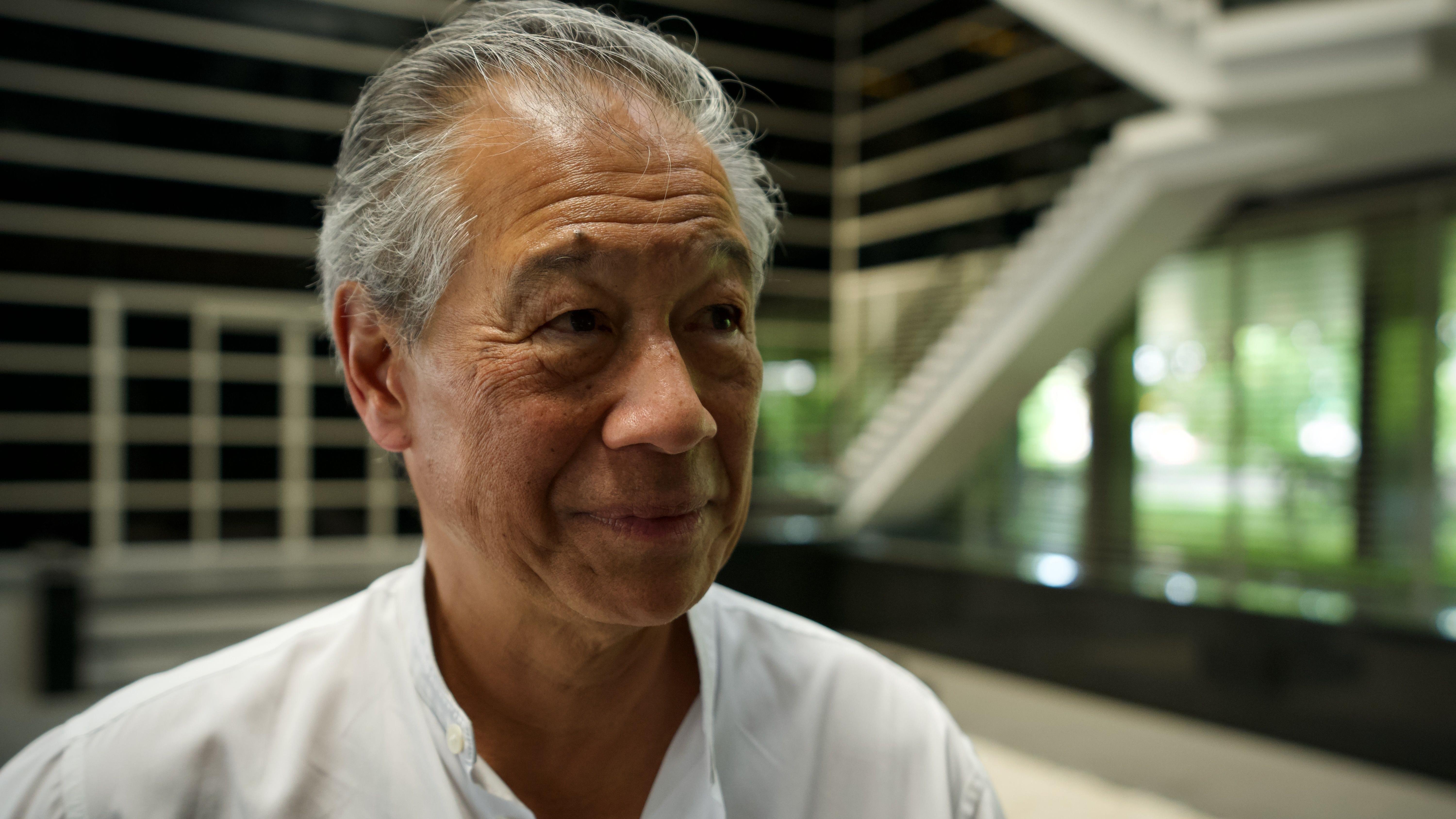 白髮的理查德·韓在接受BBC採訪時微笑著。他身穿白色襯衫。