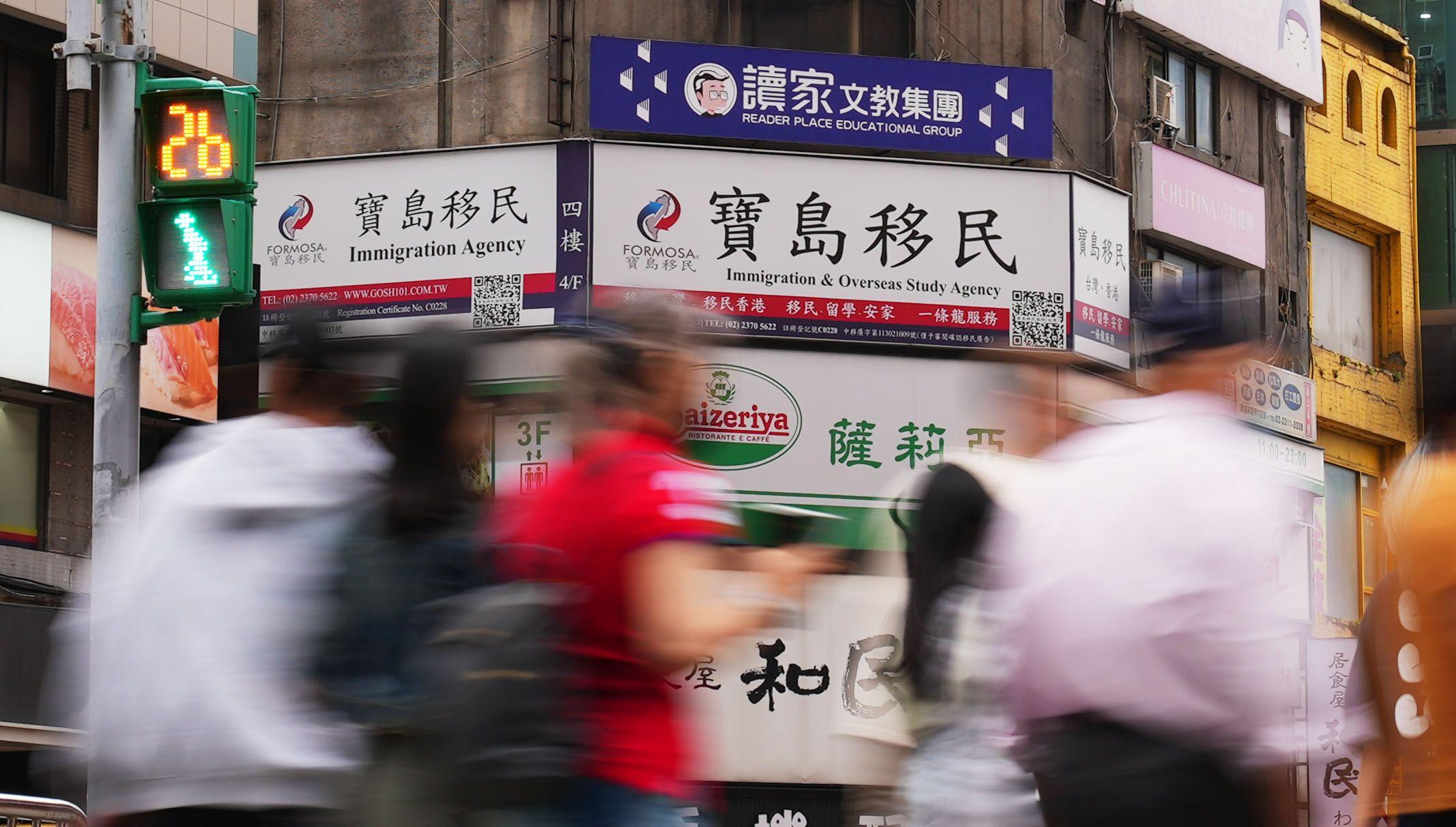 台北的街景，前景是一些行走中的路人，後面的大廈有一些廣告牌，其中一塊印有「寶島移民」字眼。