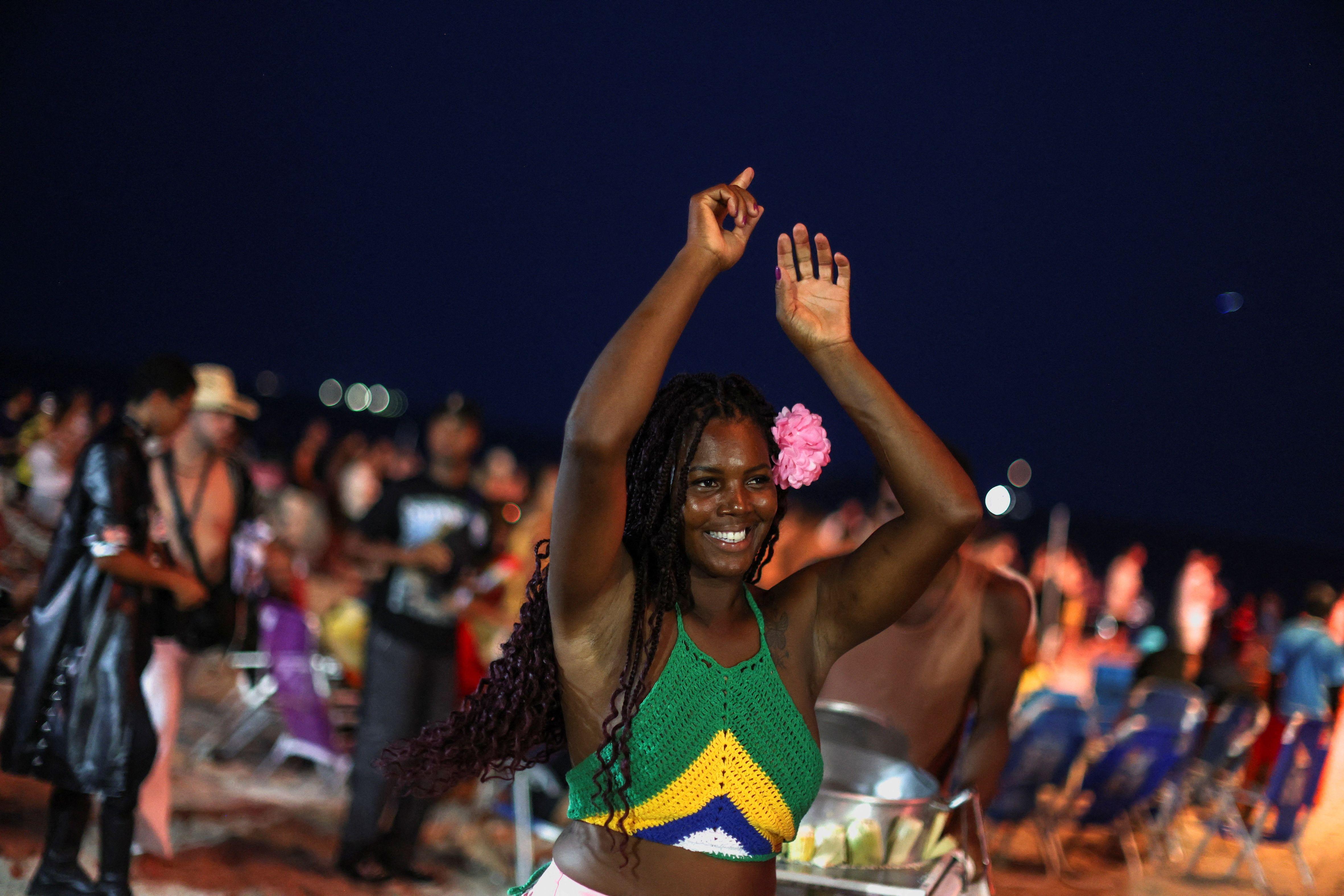 Mulher negra com blusa nas cores do Brasil. Ela levanta os bra&ccedil;os e sorri, com multid&atilde;o ao fundo