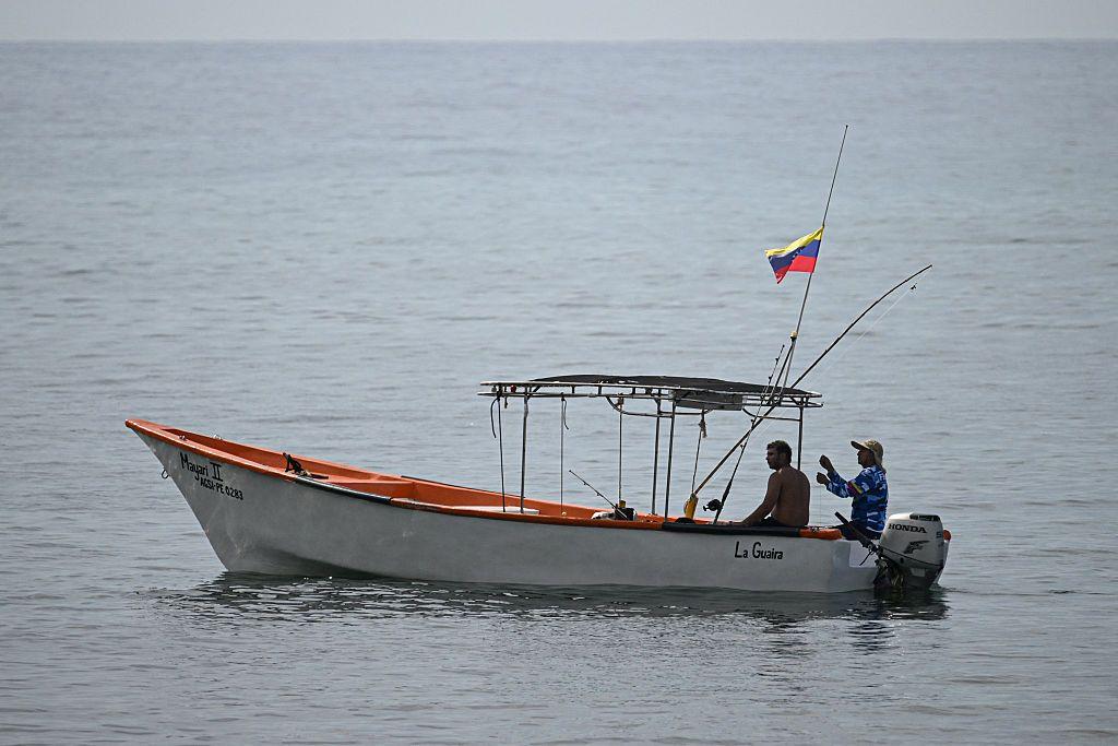 Dos pescadores navegan en un bote con la bandera de Venezuela.