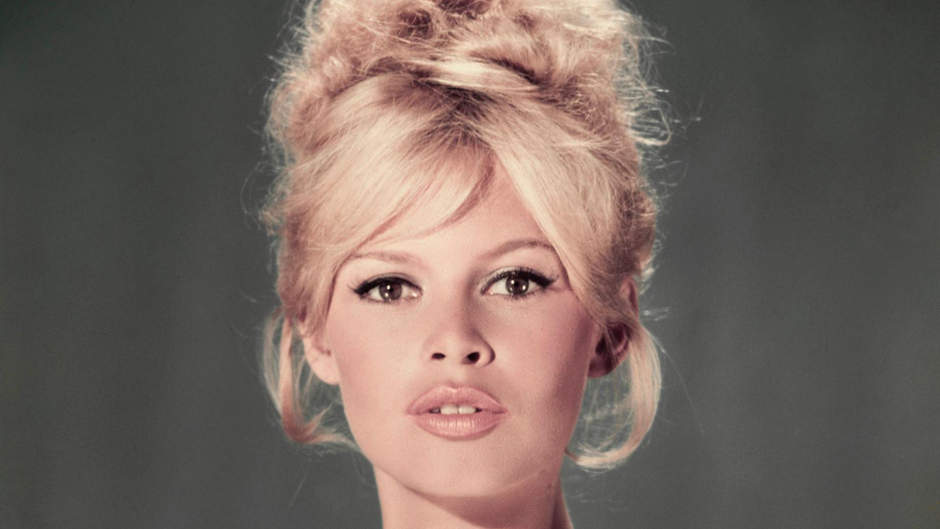Um retrato de estúdio de Brigitte Bardot usando um vestido azul claro tomara que caia com um penteado loiro estilo colmeia e os lábios ligeiramente entreabertos