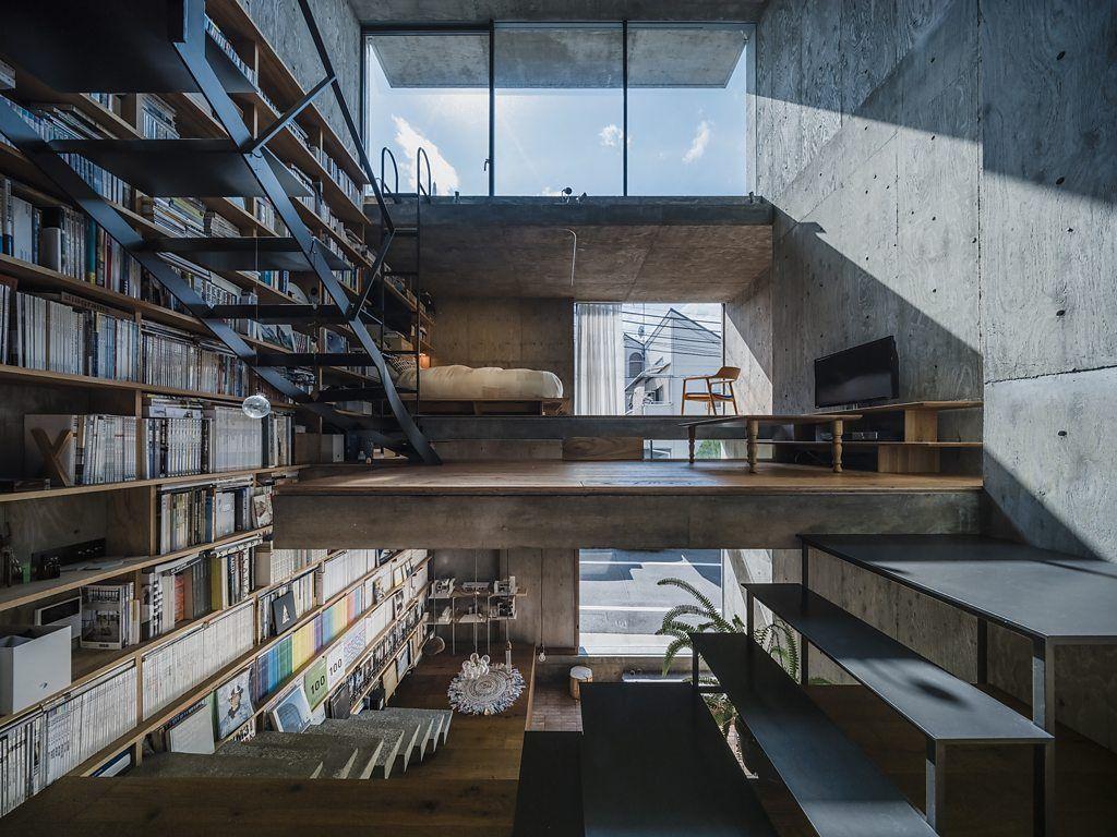 Espacio interior de estilo industrial con biblioteca de doble altura, escaleras metálicas, entrepisos de hormigón y grandes ventanales.