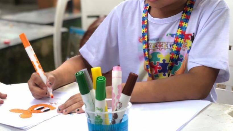 Crian&ccedil;a autista com o cord&atilde;o colorido que indica a condi&ccedil;&atilde;o colorindo com canetinhas