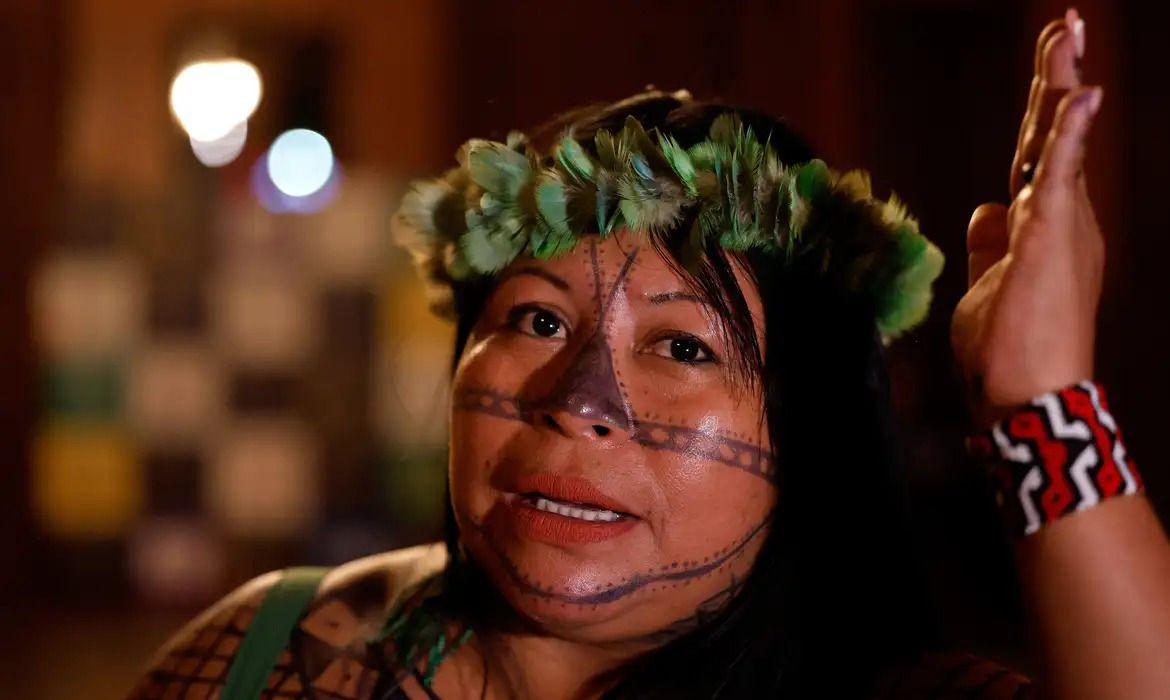 A líder indígena Alessandra Korap Munduruku com adereço de penas na cabeça, pulseira de miçangas no pulso e pinturas tradicionais no rosto e ombros