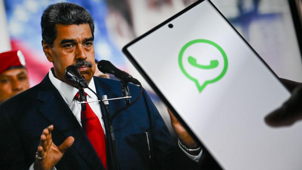 Un teléfono en el que se ve el logo de WhatsApp y detrás una foto del presidente  de Venezuela.