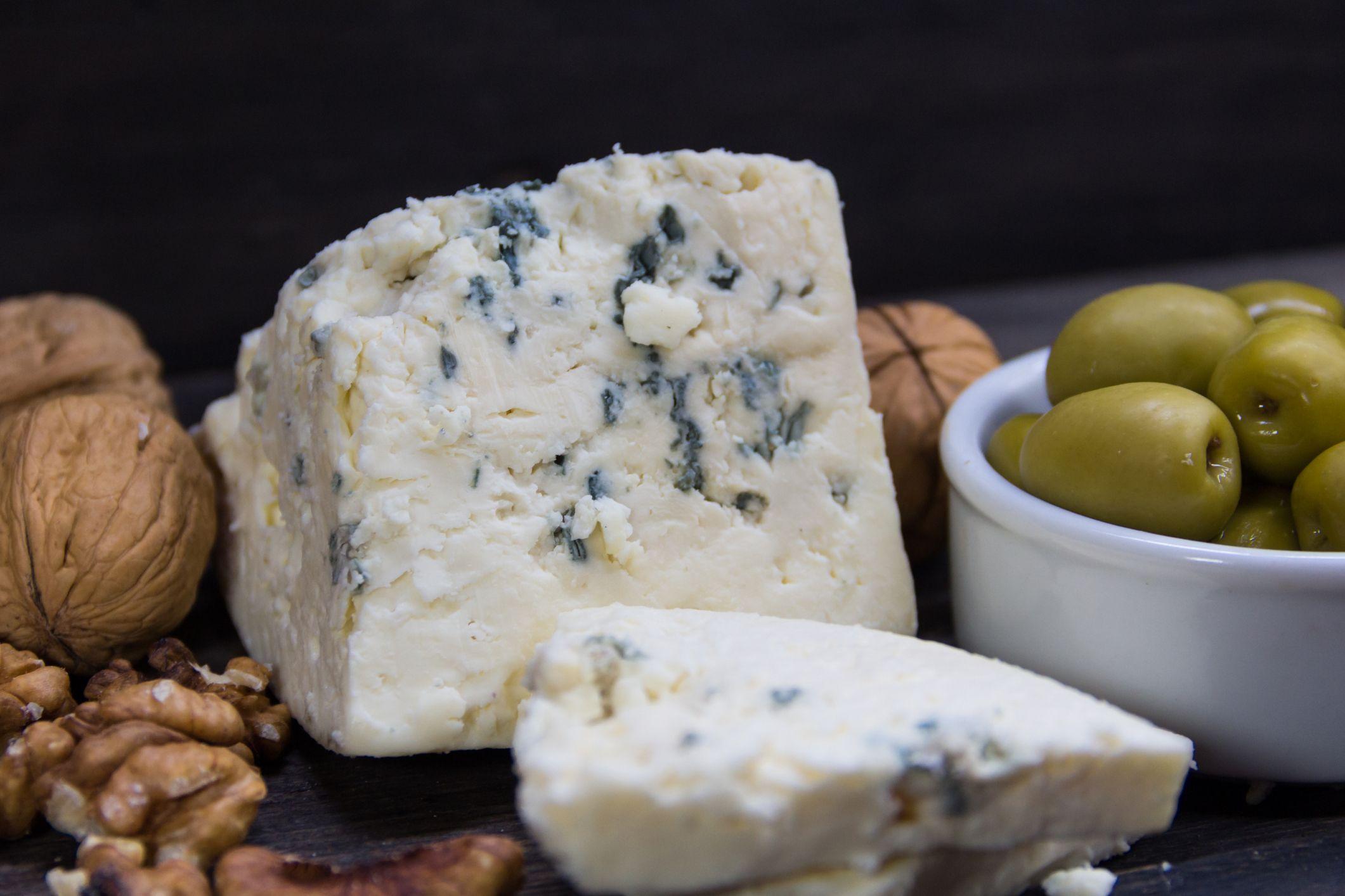 Un pedazo de queso azul como parte de una tabla con nueces de macadamia y aceitunas verdes