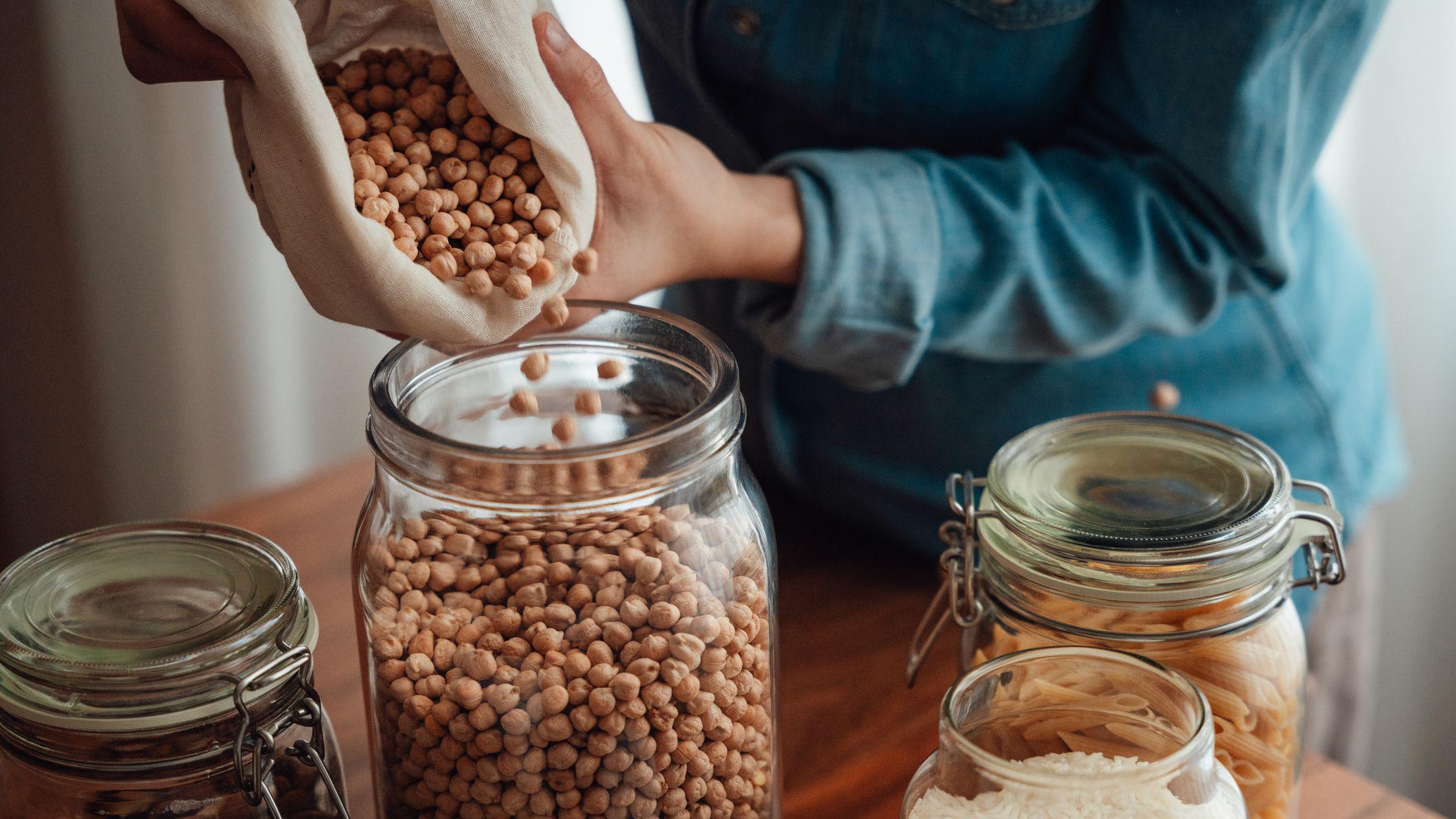 Pessoa colocando gr&atilde;os-de-bico em um frasco de vidro