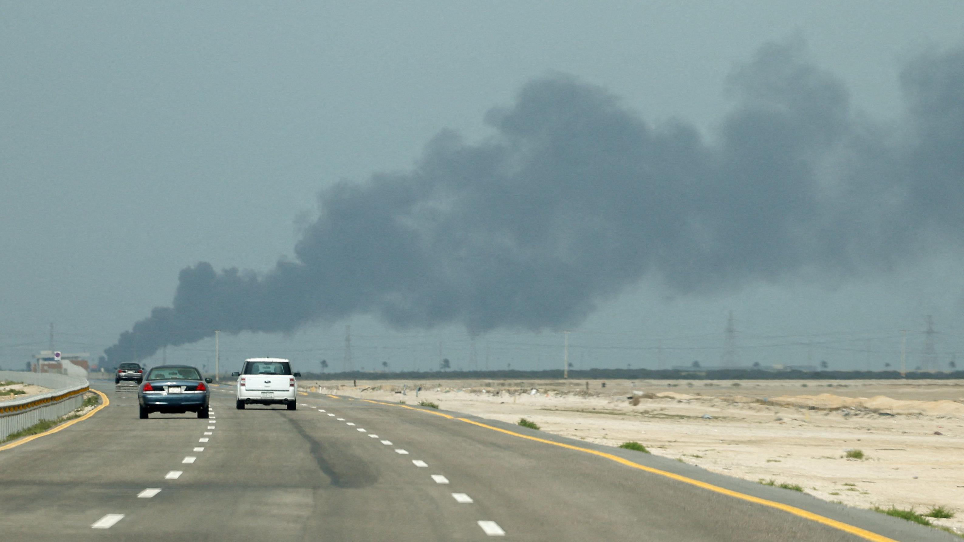 Tr&ecirc;s carros passam por uma rodovia de tr&ecirc;s faixas, com fuma&ccedil;a &agrave; frente e arbustos nas margens da estrada 