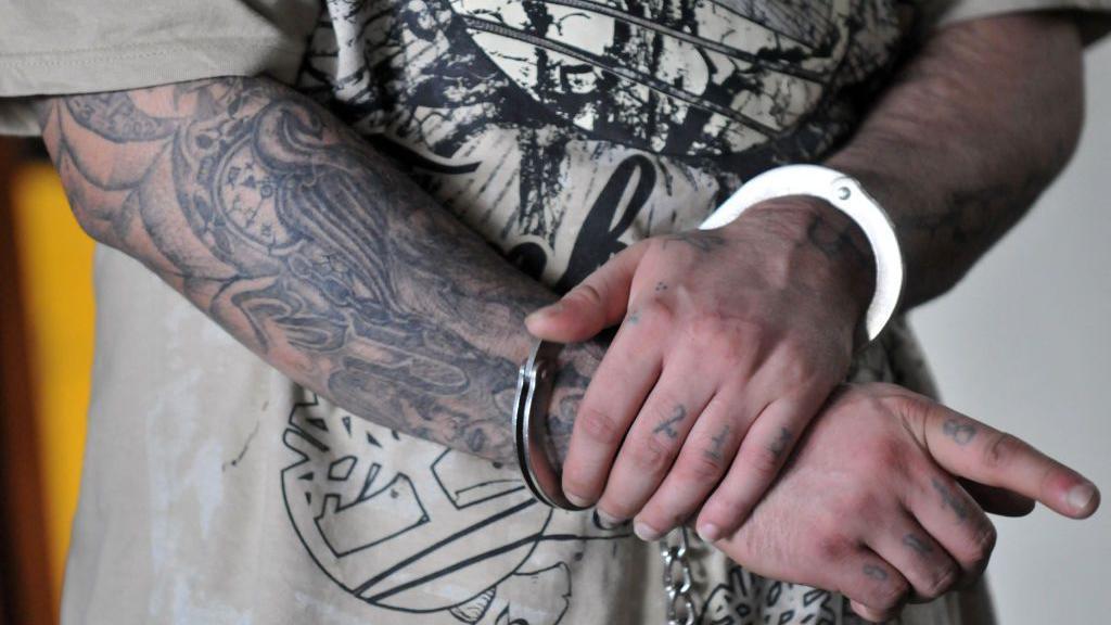 Carlos Reyes, también conocido como "Lobo", miembro de la pandilla "Mara 18", realiza gestos mientras es escoltado a la corte en Ciudad de Guatemala el 24 de agosto de 2010. Trece miembros de la pandilla enfrentan acusaciones de extorsión y asesinato de pilotos. (Foto de JOHAN ORDONEZ/AFP vía Getty Images)