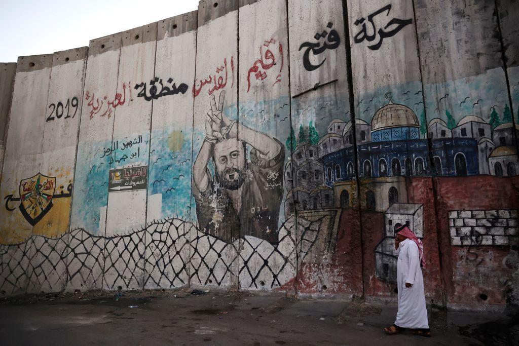 رجل فلسطيني يسير بمحاذاة جدار الفصل الإسرائيلي المرسوم عليه صورة زعيم فتح المسجون مروان البرغوثي، في بلدة العيزرية في الضفة الغربية، على مشارف القدس، في 8 نوفمبر/تشرين الثاني 2021.