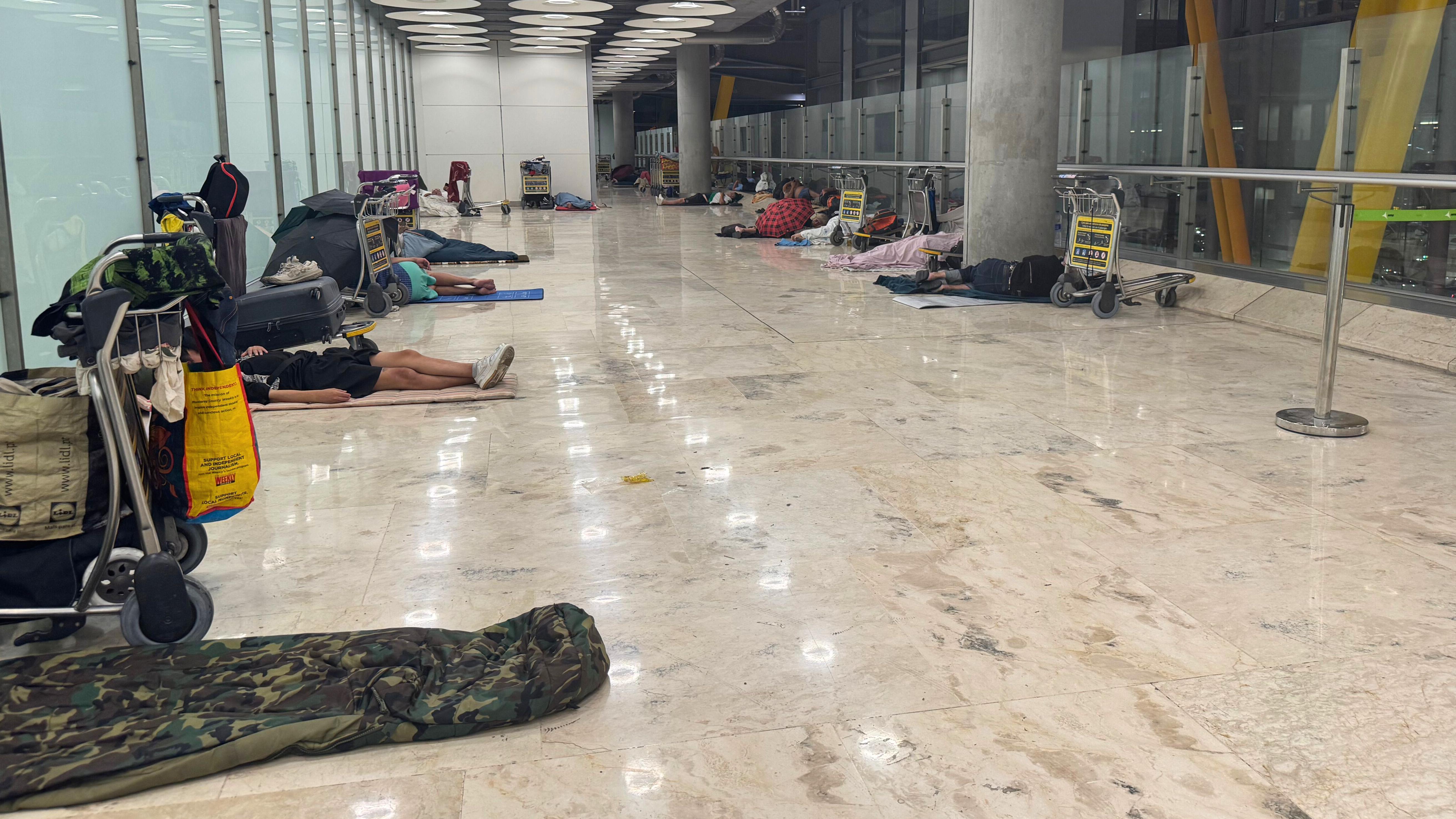 Personas durmiendo en un pasillo del aeropuerto de Barajas.