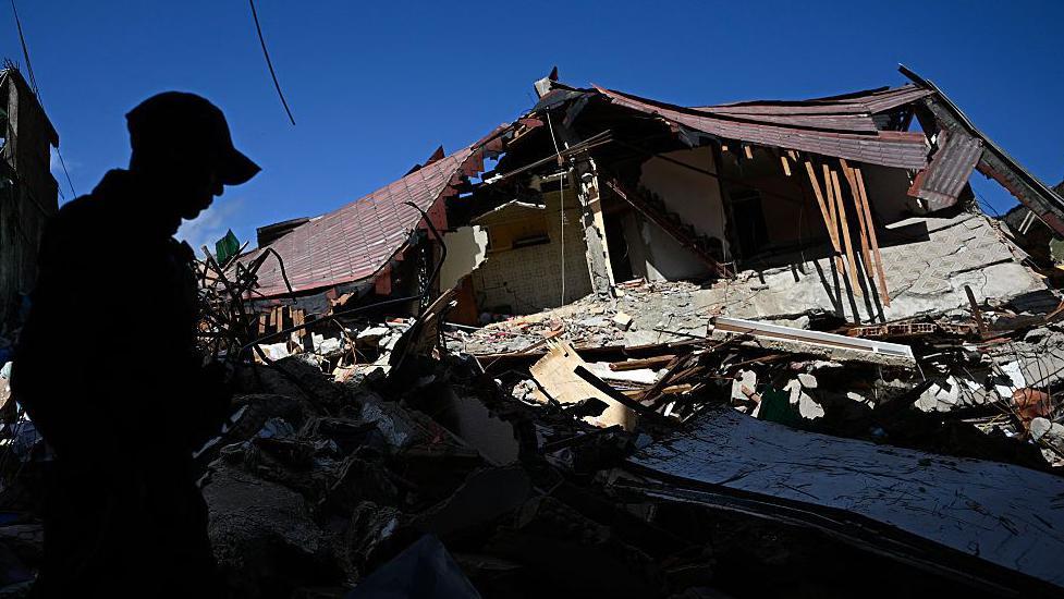 Un hombre con gorra frente a los restos de un edificio caído en El Junquito.