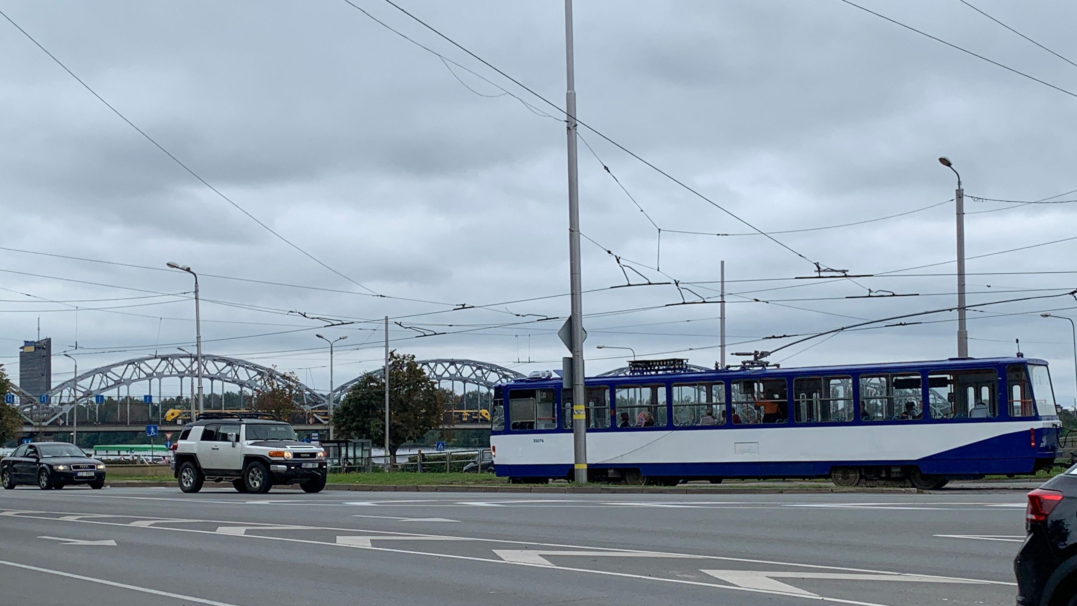 Plavo-beli tramvaj prolazi jednom od riških ulica, a u daljini se vidi jedan od 145 mostova koliko ih ima u ovom gradu