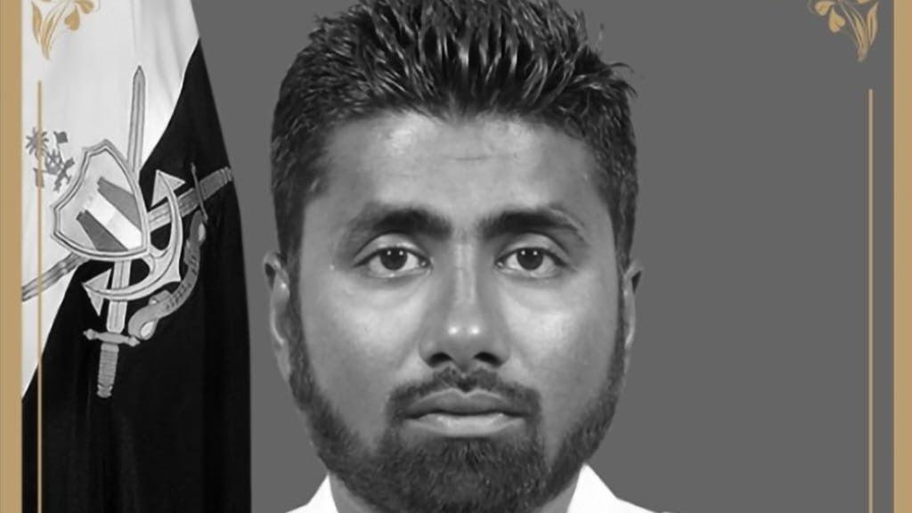 El buceador maldivo Mohamed Mahdhee, de cabello y barba oscuros, mira hacia la cámara. Detrás de él hay una bandera.