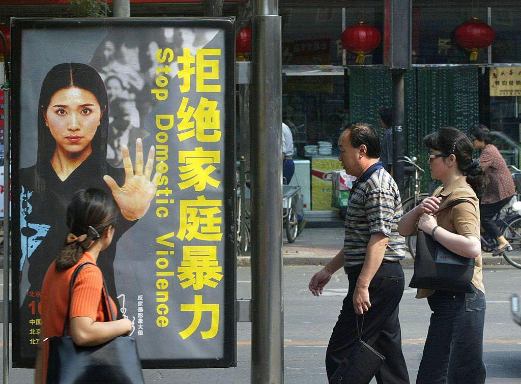 街頭上一幅印有「拒絕家庭暴力」的海報，三名途人經過。