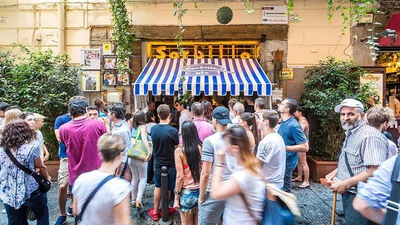 Várias pessoas na rua em frente a uma pizzaria