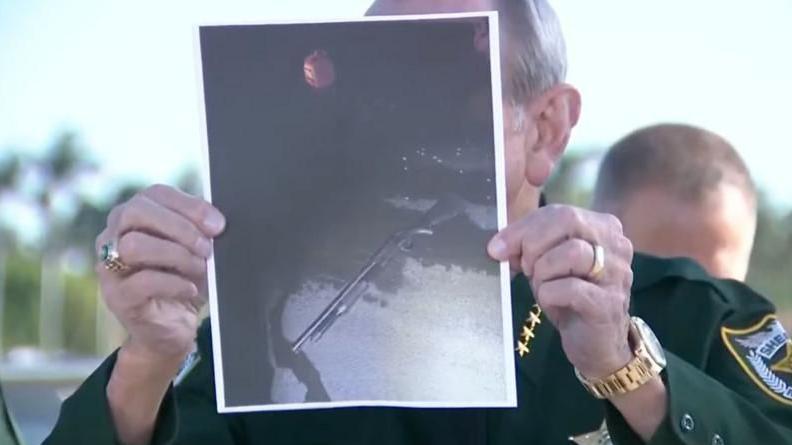 El sheriff del condado de Palm Beach, Ric Bradshaw, muestra una fotografía de la escopeta del sospechoso, con un bote de gasolina rojo visible en el fondo.