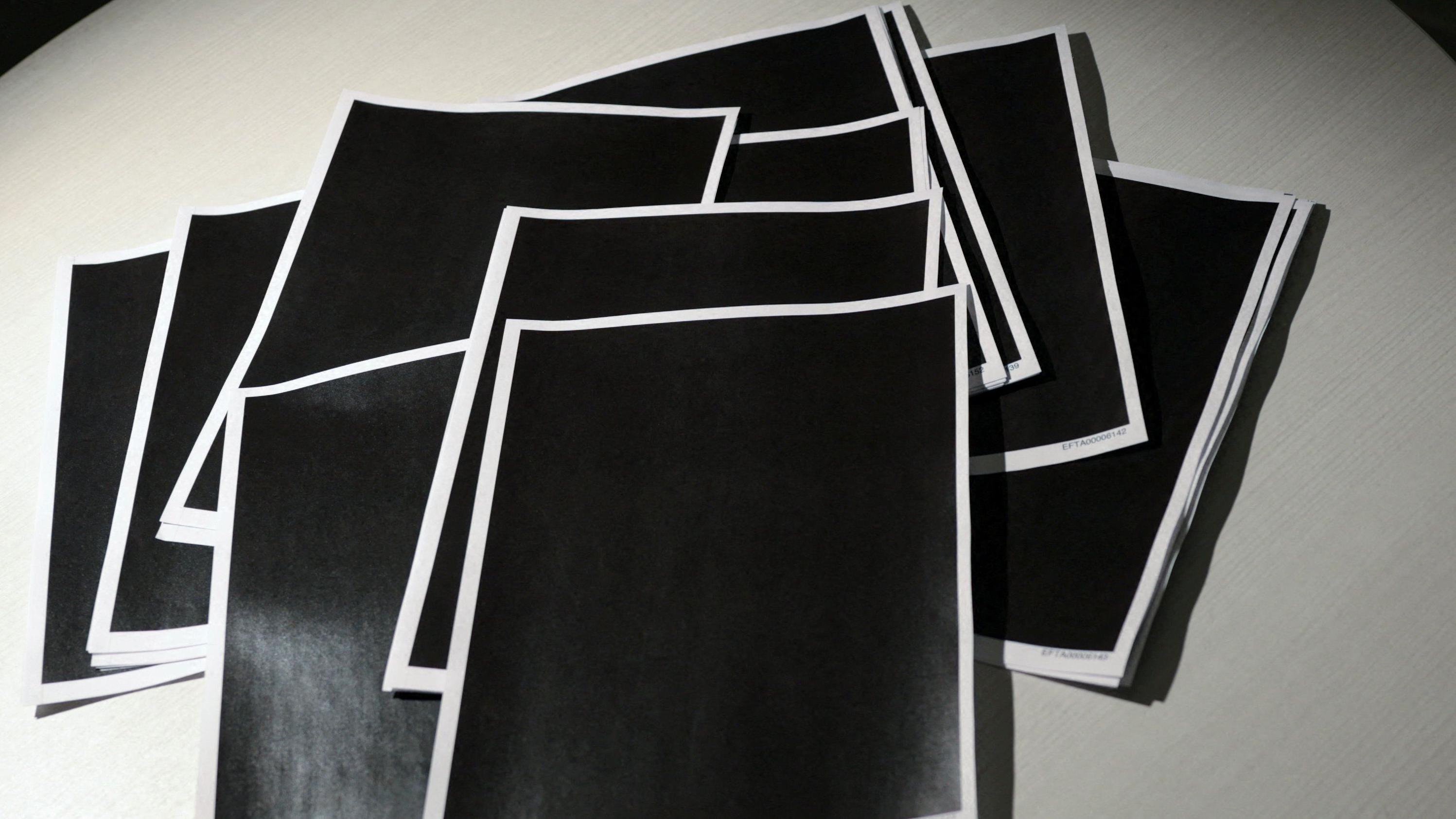 Decenas de páginas copletamente tachadas en negro yacen sobre una mesa.