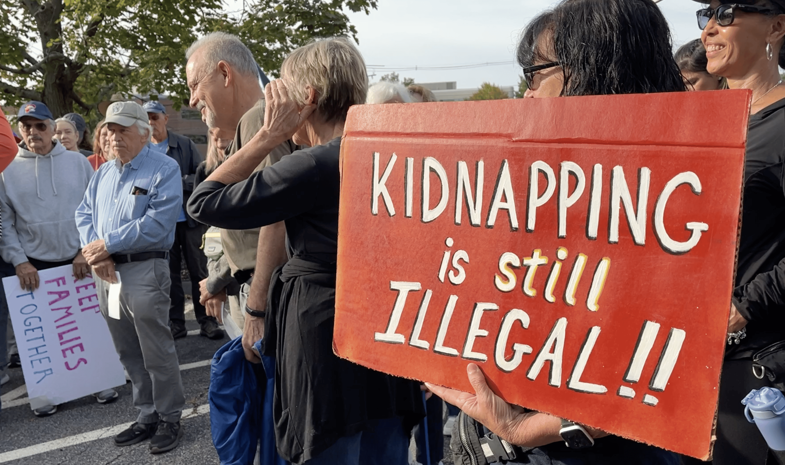 Cartaz vermelho durante manifestação contra imigração ilegal e diz: 