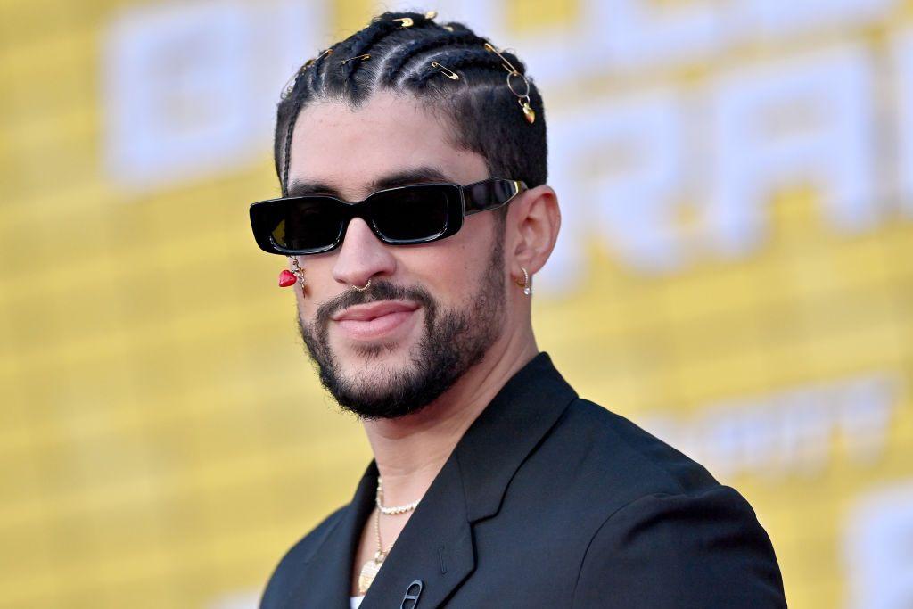 Bad Bunny sonriendo con gafas de sol negra y un pendiente.
