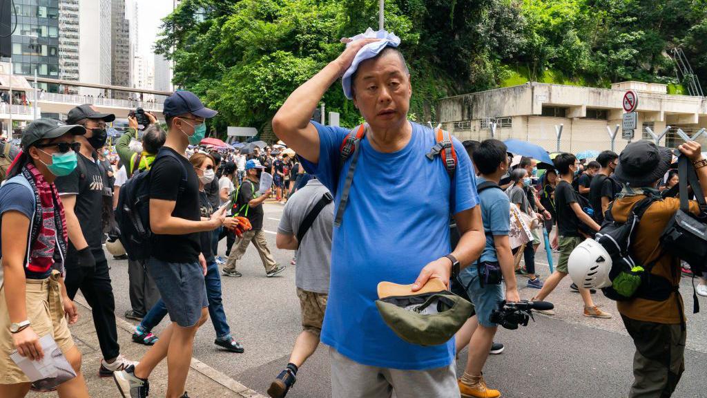 El magnate de los medios Jimmy Lai asiste a una marcha de manifestantes prodemocracia en Hong Kong, China. Luce una camiseta azul y en la mano tiene una gorra.