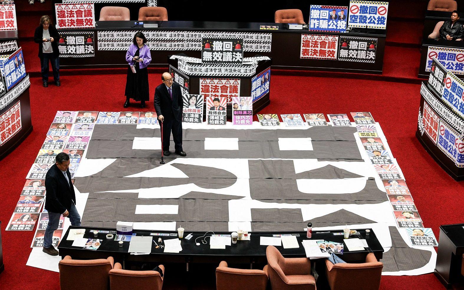 2025年3月28日，執政民進黨立委柯建銘站在立法院一張寫有「罷免」字樣的海報上