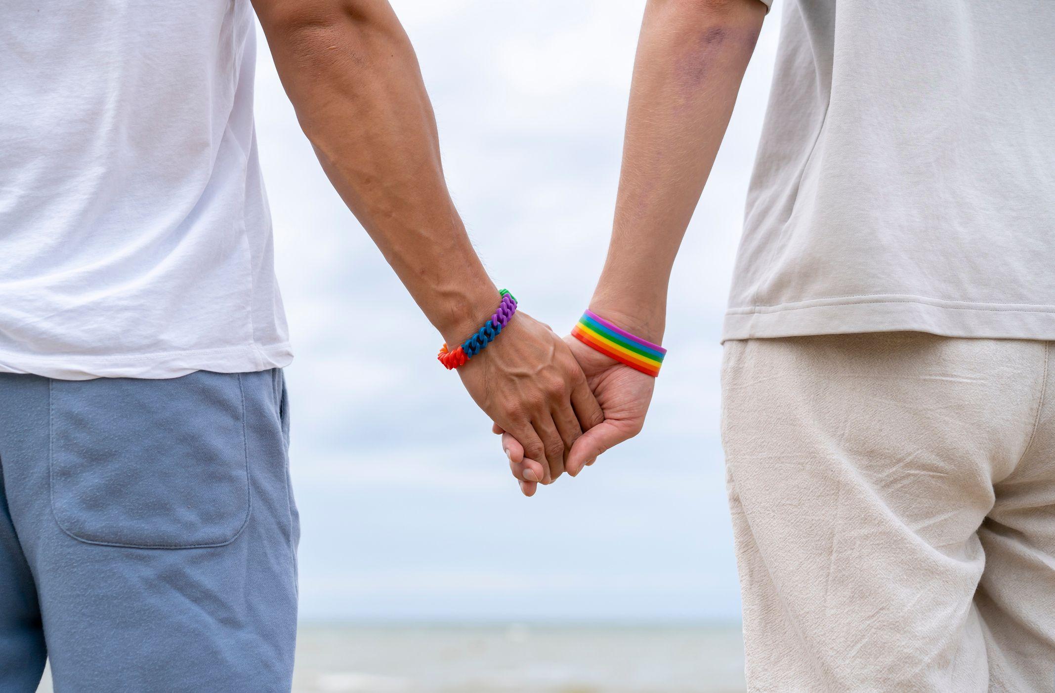 Una pareja homosexual se agarra de la mano frente a la playa.