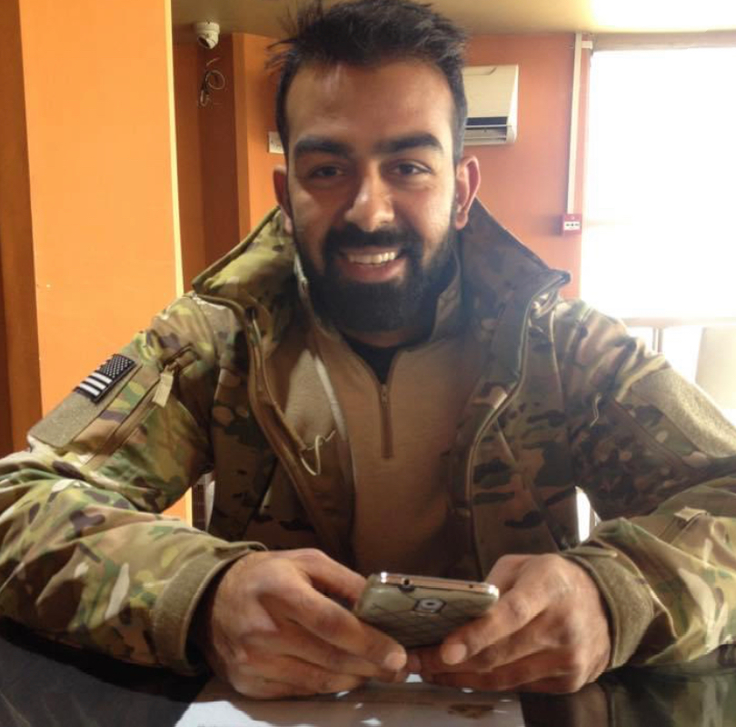 Safi in military uniform smiling at the camera while holding a phone