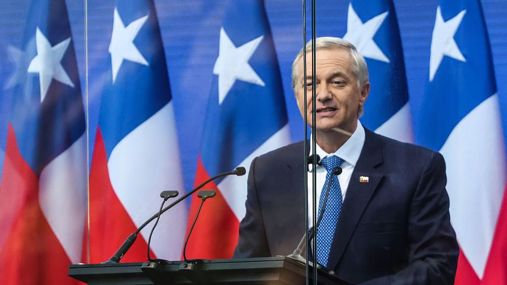 José Antonio Kast se dirige a adherentes en su cierre de camapaña. Lo hace detrás de un vidrio antibalas y con banderas de Chile en sus espaldas. 