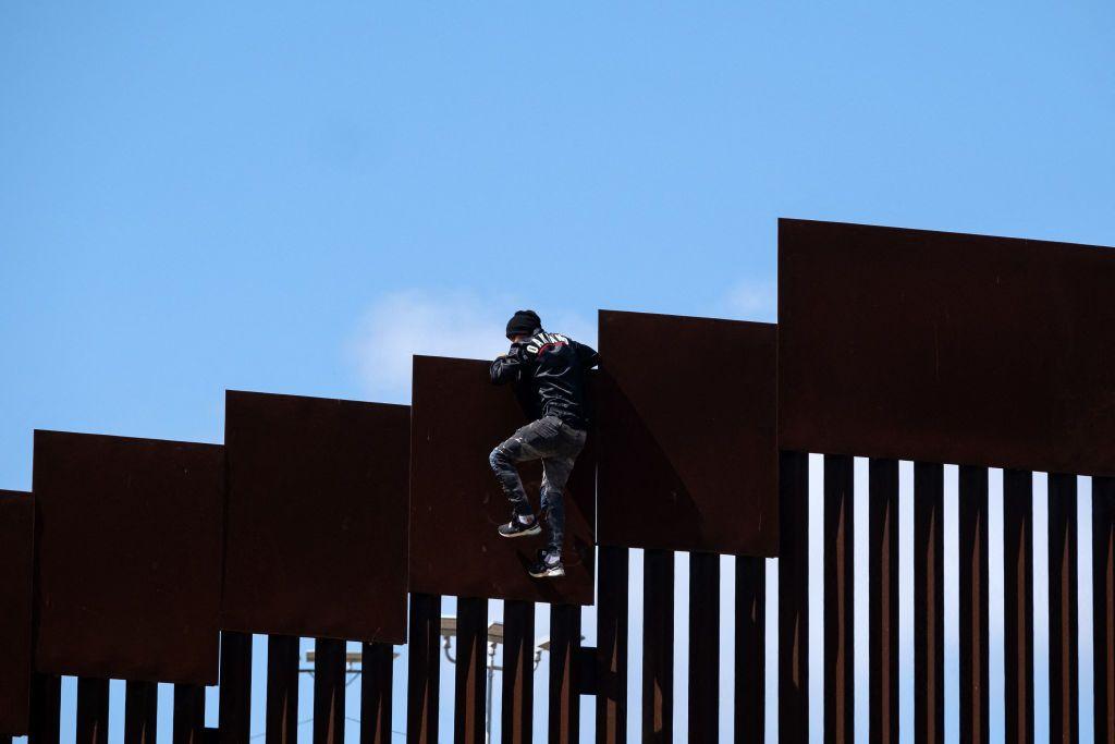 Migrante encima del muro de la frontera entre México y EE.UU