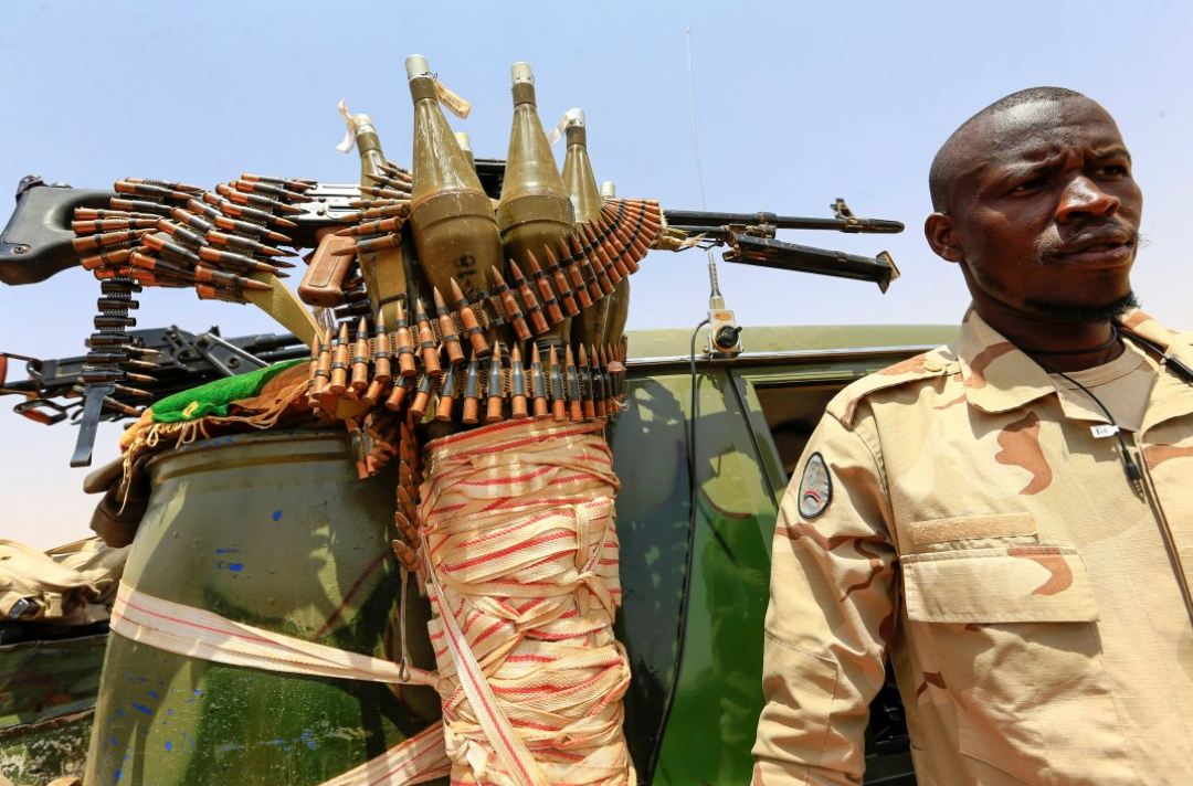 يقف أحد أفراد قوات الدعم السريع شبه العسكرية السودانية بجوار مركبة أثناء عملية لتحديد مكان المهاجرين غير النظاميين واعتقالهم الذين تخلى عنهم المتاجرون في منطقة صحراوية نائية بالقرب من الحدود الليبية ونقلهم إلى حدود ولاية الخرطوم.
