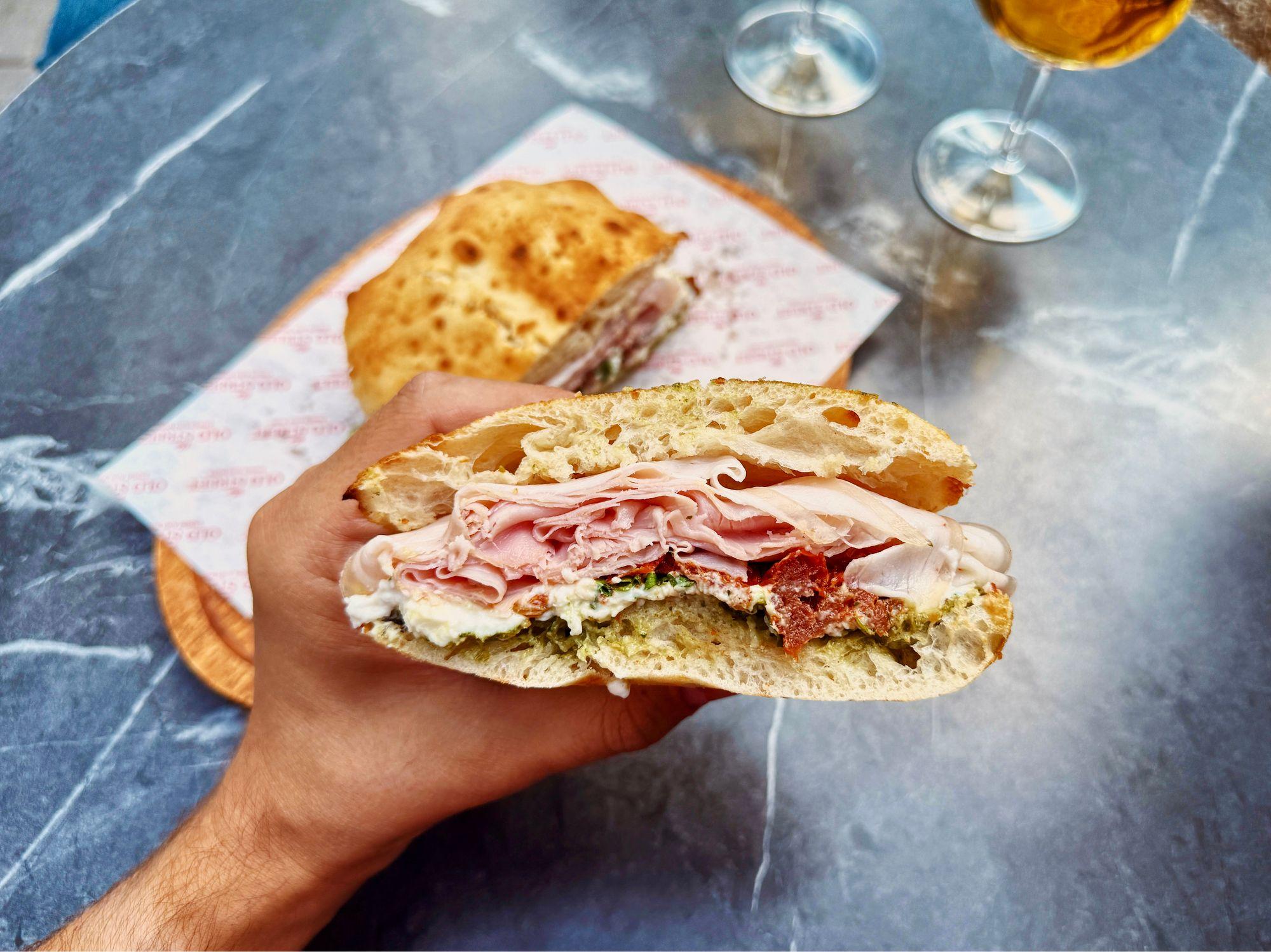 Una persona tiene un sándwich con jamón y otros productos en la mano